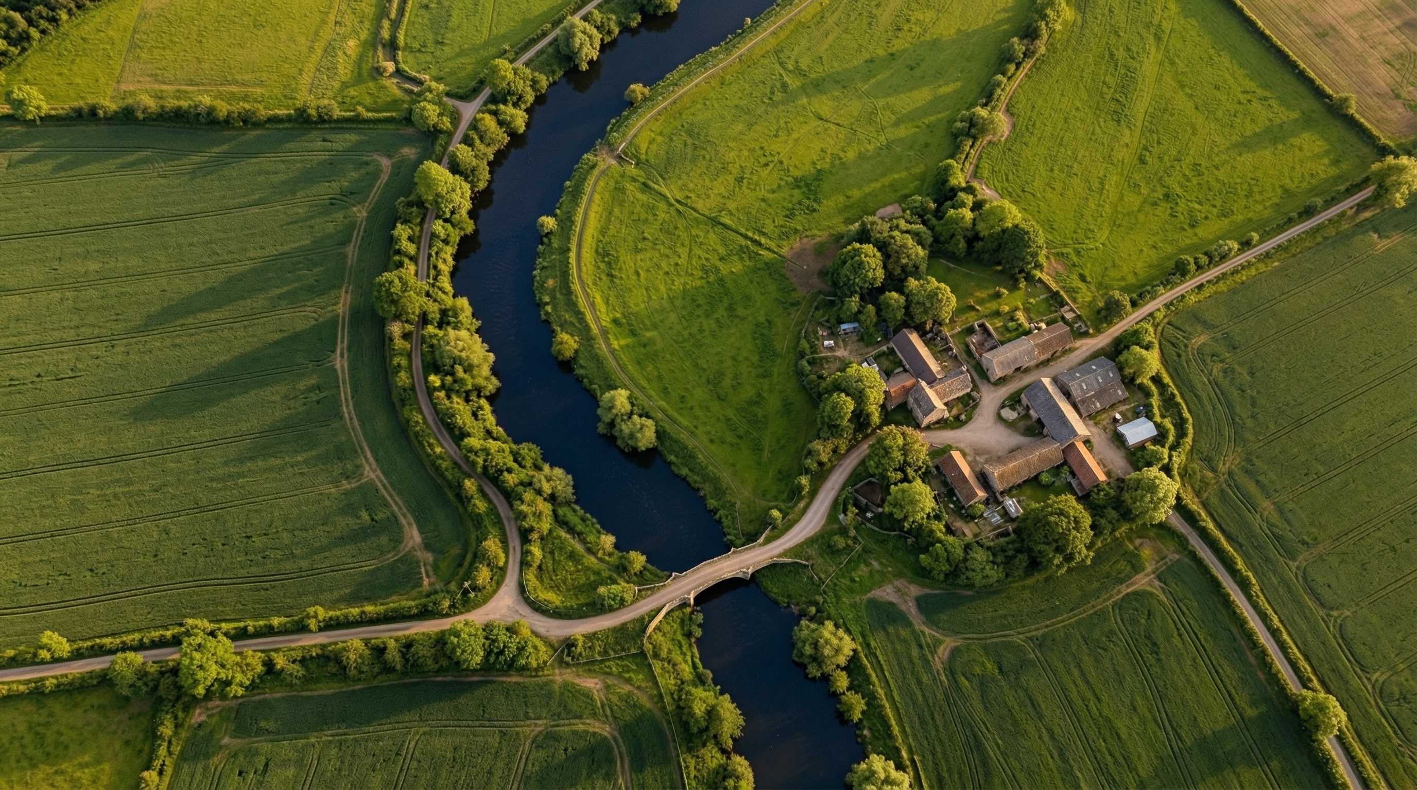 A winding river through green farmland with a small bridge